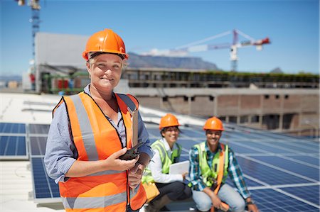 simsearch:6113-06753315,k - Portrait smiling, confident female engineer with walkie-talkie at sunny solar power plant Fotografie stock - Premium Royalty-Free, Codice: 6113-09157830