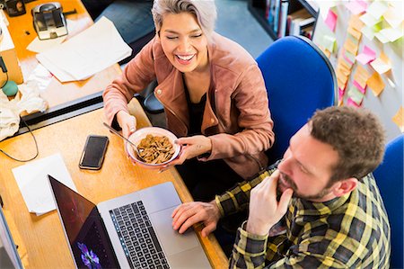 Creative business people eating cereal, working at laptop on office Stock Photo - Premium Royalty-Free, Code: 6113-09160011