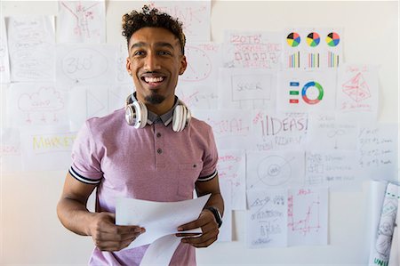 portrait of smiling casual businessman with paperwork in office - Portrait smiling, confident creative businessman hanging paperwork on office wall Photographie de stock - Premium Libres de Droits, Code: 6113-09160039