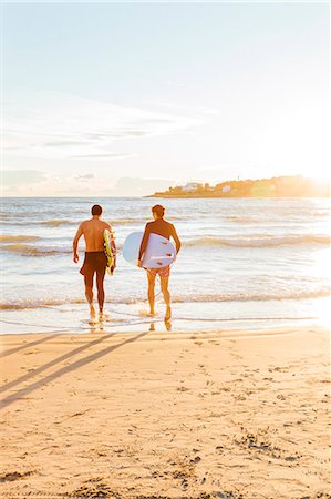 simsearch:6113-09168363,k - Male surfers carrying surfboards into ocean on sunny beach Photographie de stock - Premium Libres de Droits, Code: 6113-09168355