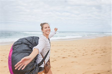 parachute, beach - Portrait smiling, carefree young female paraglider with parachute backpack on ocean beach Photographie de stock - Premium Libres de Droits, Code: 6113-09168455