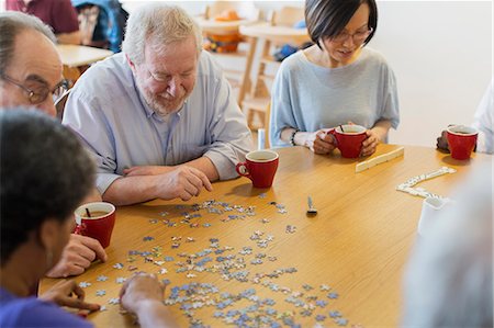 Senior friends assembling jigsaw puzzle and drinking tea at table in community center Stock Photo - Premium Royalty-Free, Code: 6113-09168410