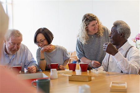 Volunteer talking with senior man playing games at table in community center Stock Photo - Premium Royalty-Free, Code: 6113-09168417