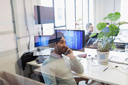 Indian computer programmer in turban talking on smart phone in office Stock Photo - Premium Royalty-Free, Code: 6113-09178688