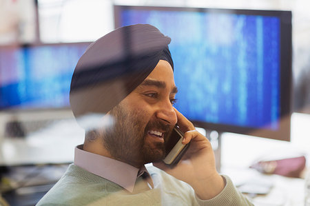 Indian computer programmer in turban talking on smart phone in office Stock Photo - Premium Royalty-Free, Code: 6113-09178691