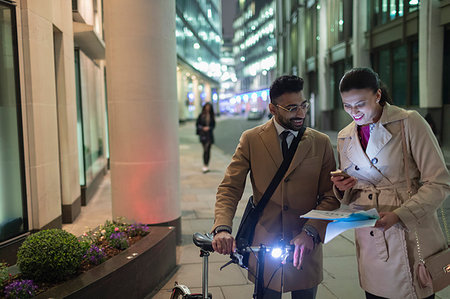 Business people with smart phone and bicycle reviewing paperwork on urban street at night Stock Photo - Premium Royalty-Free, Code: 6113-09178751