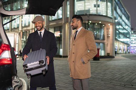 Businessmen loading suitcase into car on urban street corner at night Stock Photo - Premium Royalty-Free, Code: 6113-09178759