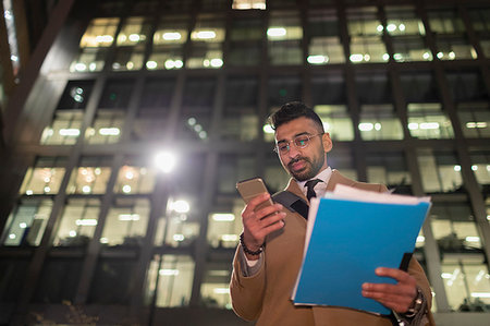 social place - Businessman with paperwork and smart phone below urban highrise at night Stock Photo - Premium Royalty-Free, Code: 6113-09178769