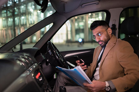 Businessman with smart phone reading paperwork in car at night Stock Photo - Premium Royalty-Free, Code: 6113-09178829
