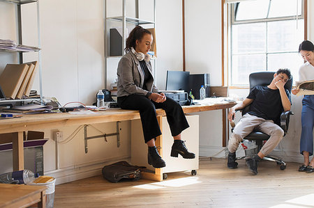 Creative businesswoman with headphones sitting on desk in office Stock Photo - Premium Royalty-Free, Code: 6113-09179133