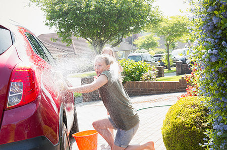 simsearch:6113-06720878,k - Playful daughter spraying mother with hose, washing car in sunny driveway Foto de stock - Sin royalties Premium, Código: 6113-09191931