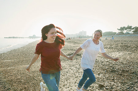 Playful, affectionate lesbian couple holding hands and running on sunny beach Stock Photo - Premium Royalty-Free, Code: 6113-09199751