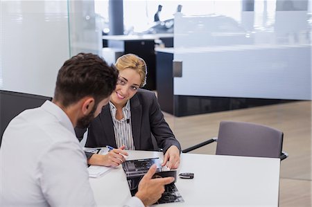 Smiling car saleswoman showing brochure to male customer in car dealership office Stock Photo - Premium Royalty-Free, Code: 6113-09111800