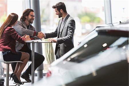 Car salesman handshaking with couple customers at table in car dealership showroom Stock Photo - Premium Royalty-Free, Code: 6113-09111806