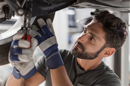 Focused male mechanic fixing wheel underneath car in auto repair shop Stock Photo - Premium Royalty-Free, Code: 6113-09111809