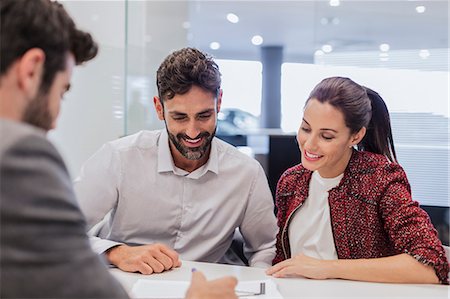 Car salesman explaining financial contract paperwork to couple customers in car dealership office Stock Photo - Premium Royalty-Free, Code: 6113-09111813