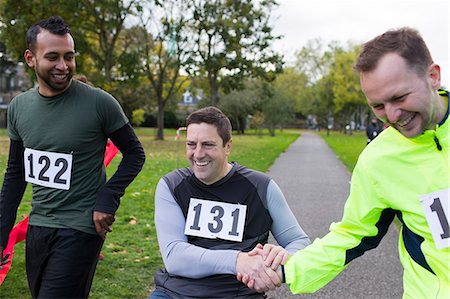 simsearch:6113-09131399,k - Smiling male runner shaking hands with friend in wheelchair at charity race in park Foto de stock - Royalty Free Premium, Número: 6113-09131280