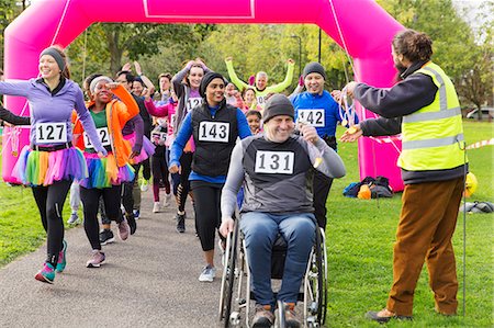 Man in wheelchair and runners receiving medals, crossing charity race finish line Stock Photo - Premium Royalty-Free, Code: 6113-09131423