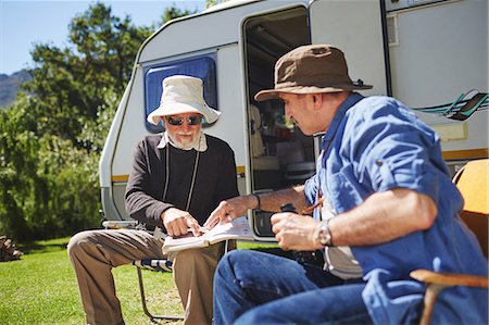 Senior men friends looking at guidebook outside camper van at sunny summer campsite Fotografie stock - Premium Royalty-Free, Codice: 6113-09131506