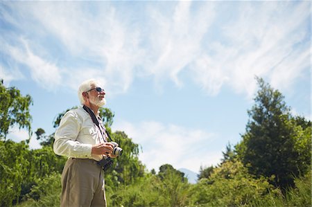 Curious active senior man with digital camera looking up at sunny trees and sky Stock Photo - Premium Royalty-Free, Code: 6113-09131523