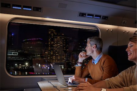 Businessman working at laptop on passenger train at night, looking out window at passing city Stock Photo - Premium Royalty-Free, Code: 6113-09131605