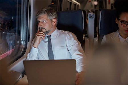 Serious, thoughtful businessman working at laptop, looking out window on passenger train at night Stock Photo - Premium Royalty-Free, Code: 6113-09131611