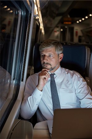 simsearch:6124-08520395,k - Serious, thoughtful businessman working at laptop, looking out window on passenger train at night Stock Photo - Premium Royalty-Free, Code: 6113-09131614