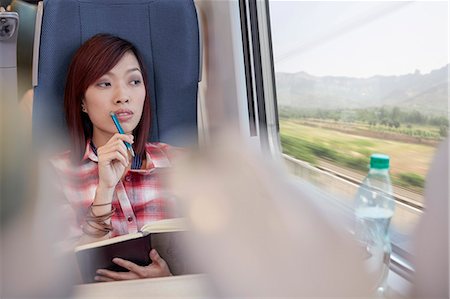 Thoughtful young woman writing in journal and looking out window on passenger train Stock Photo - Premium Royalty-Free, Code: 6113-09131629