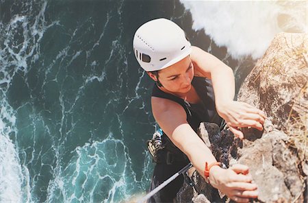 simsearch:700-01344830,k - Determined, focused female rock climber hanging from rock above sunny ocean Stock Photo - Premium Royalty-Free, Code: 6113-09131785