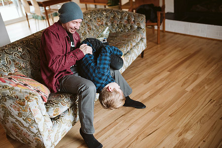 simsearch:6108-08663387,k - Playful father holding son upside-down on living room sofa Foto de stock - Sin royalties Premium, Código: 6113-09240142