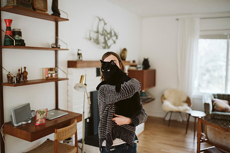 Girl holding black cat in living room Stock Photo - Premium Royalty-Free, Code: 6113-09240156