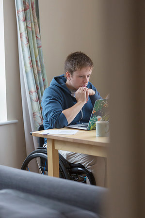 studying drinking coffee - Focused young woman in wheelchair using laptop at dining table Stock Photo - Premium Royalty-Free, Code: 6113-09240685