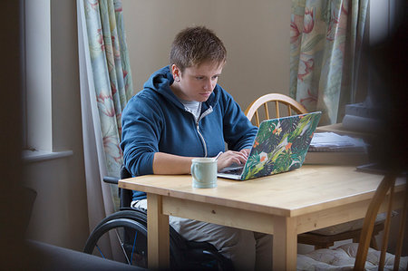 simsearch:6113-09240477,k - Focused young woman in wheelchair using laptop at dining table Foto de stock - Royalty Free Premium, Número: 6113-09240778