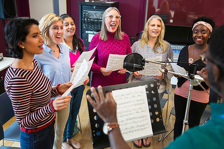 simsearch:6113-09168289,k - Male conductor leading womens choir with sheet music singing in music recording studio Stock Photo - Premium Royalty-Free, Code: 6113-09240878