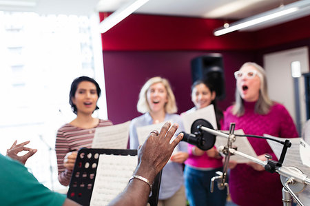 simsearch:6113-09168289,k - Male conductor leading womens choir with sheet music singing in music recording studio Stock Photo - Premium Royalty-Free, Code: 6113-09240885