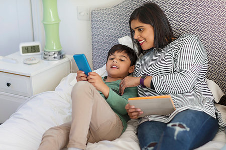 Mother and son using smart phone and digital tablet on bed Stock Photo - Premium Royalty-Free, Code: 6113-09241110