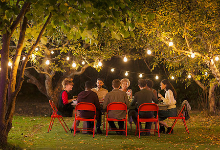 Friends enjoying dinner garden party under trees with fairy lights Stock Photo - Premium Royalty-Free, Code: 6113-09241345