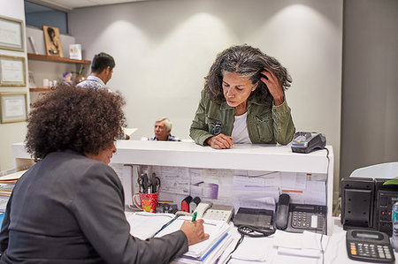 person reading at desk - Female patient rescheduling with receptionist in clinic Stock Photo - Premium Royalty-Free, Code: 6113-09241575