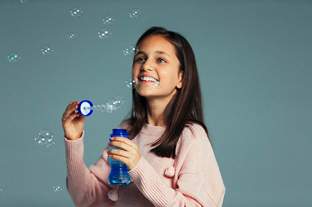 simsearch:6118-07966899,k - Happy, playful girl with bubble wand blowing bubbles Stock Photo - Premium Royalty-Free, Code: 6113-09272516