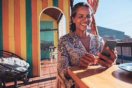 simsearch:614-08031039,k - Smiling, happy woman using smart phone on sunny restaurant balcony Stock Photo - Premium Royalty-Free, Code: 6113-09272715