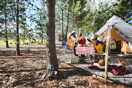 simsearch:6113-09272797,k - Lesbian couple and kids toasting mugs at sunny campsite table in woods Fotografie stock - Premium Royalty-Free, Codice: 6113-09272884