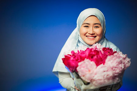 Portrait smiling, confident young woman in hijab holding pink peonies Stock Photo - Premium Royalty-Free, Code: 6113-09220461