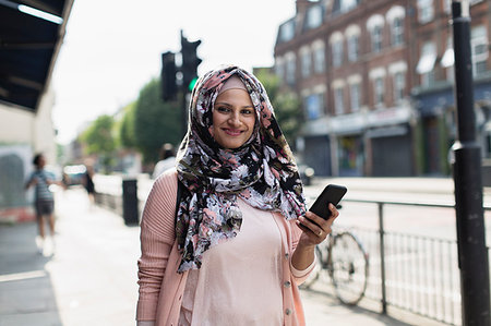 simsearch:6113-09220518,k - Portrait smiling, confident woman with smart phone wearing floral hijab on urban sidewalk Stock Photo - Premium Royalty-Free, Code: 6113-09220478
