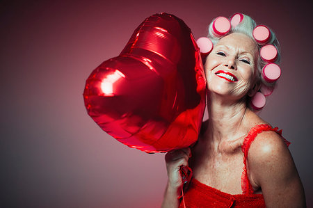 Portrait playful senior woman with hair in curlers holding heart-shape balloon Fotografie stock - Premium Royalty-Free, Codice: 6113-09220558