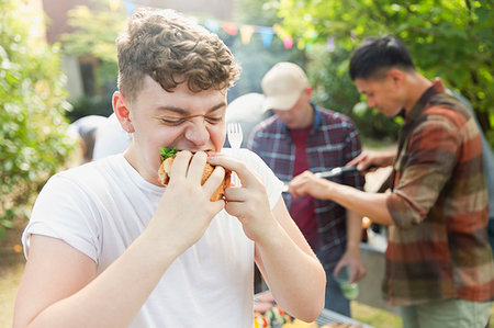 Hungry teenage boy eating hamburger at backyard barbecue Stock Photo - Premium Royalty-Free, Code: 6113-09239764