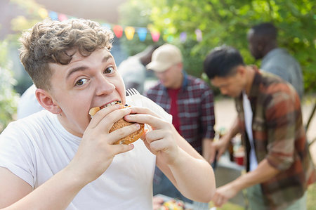 Portrait hungry teenage boy eating hamburger at backyard barbecue Stock Photo - Premium Royalty-Free, Code: 6113-09239772