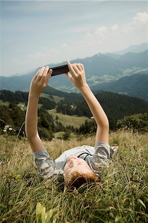 Germany, Bavaria, Boy lying on back in mountains uses a smart phone Foto de stock - Sin royalties Premium, Código: 6115-06733175