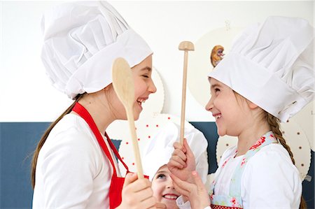 Three little girls with chef's hat and wooden spoons, Munich, Bavaria, Germany Stock Photo - Premium Royalty-Free, Code: 6115-06966914