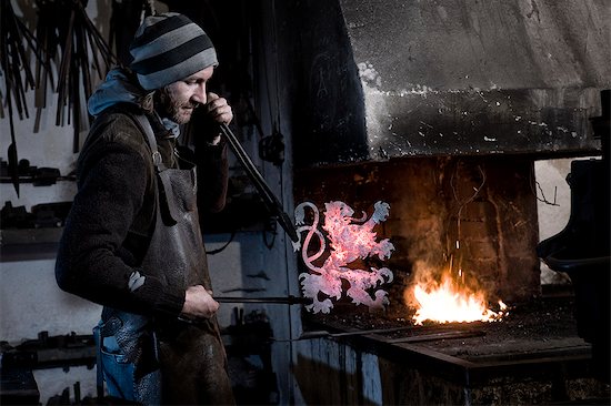 Blacksmith making coat of arms from iron, forge in background, Landshut, Bavaria, Germany Stock Photo - Premium Royalty-Free, Image code: 6115-06967124