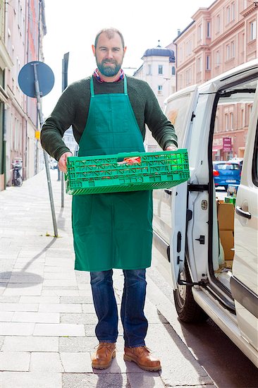 Grocer carrying food in crate by greengrocer's shop Stock Photo - Premium Royalty-Free, Image code: 6115-08149284